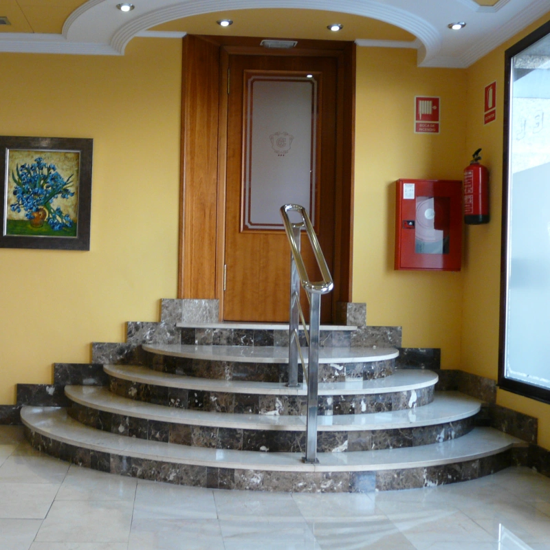 Escalera curva de m&aacute;rmol con barandilla met&aacute;lica en un vest&iacute;bulo amarillo