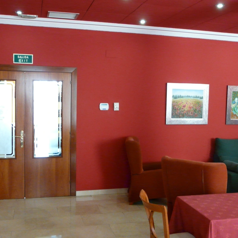 Sala roja con puerta, letrero de salida y sill&oacute;n con mesa junto a cuadros.