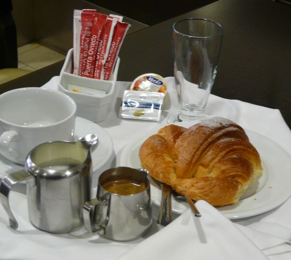 Desayuno con croissant, leche en jarra, taza, caf&eacute; y sobres en la mesa