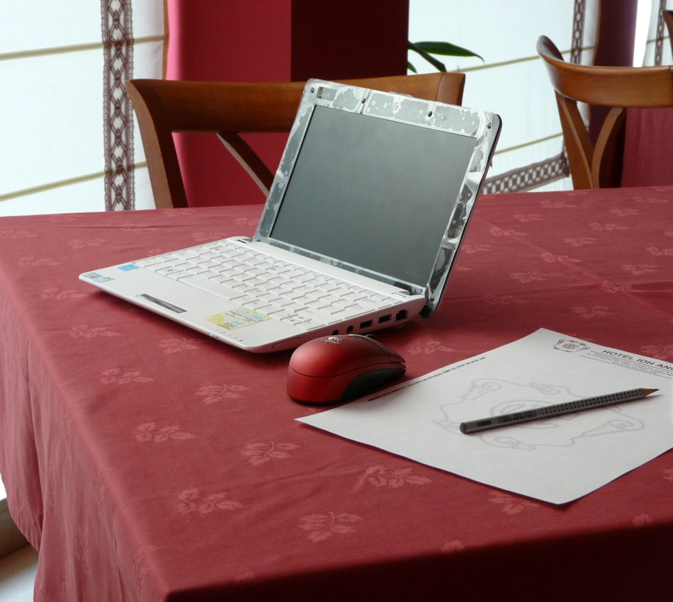 Port&aacute;til abierto y mouse sobre mesa con documentos en hotel, sala con sillas.