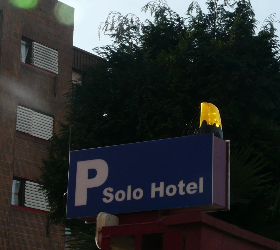 Cartel &ldquo;Solo Hotel&rdquo; con fachada de ladrillo y &aacute;rboles al fondo