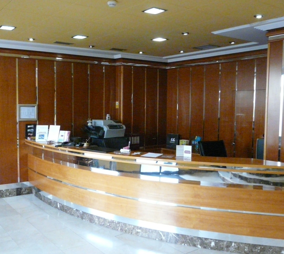 Recepci&oacute;n de oficina con mostrador de madera, equipo y luces en el techo