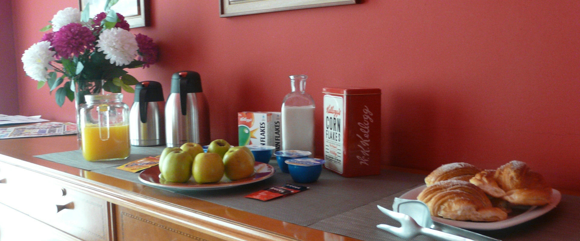 Desayuno con jugo, frutas, croissants y recipientes en mesa roja