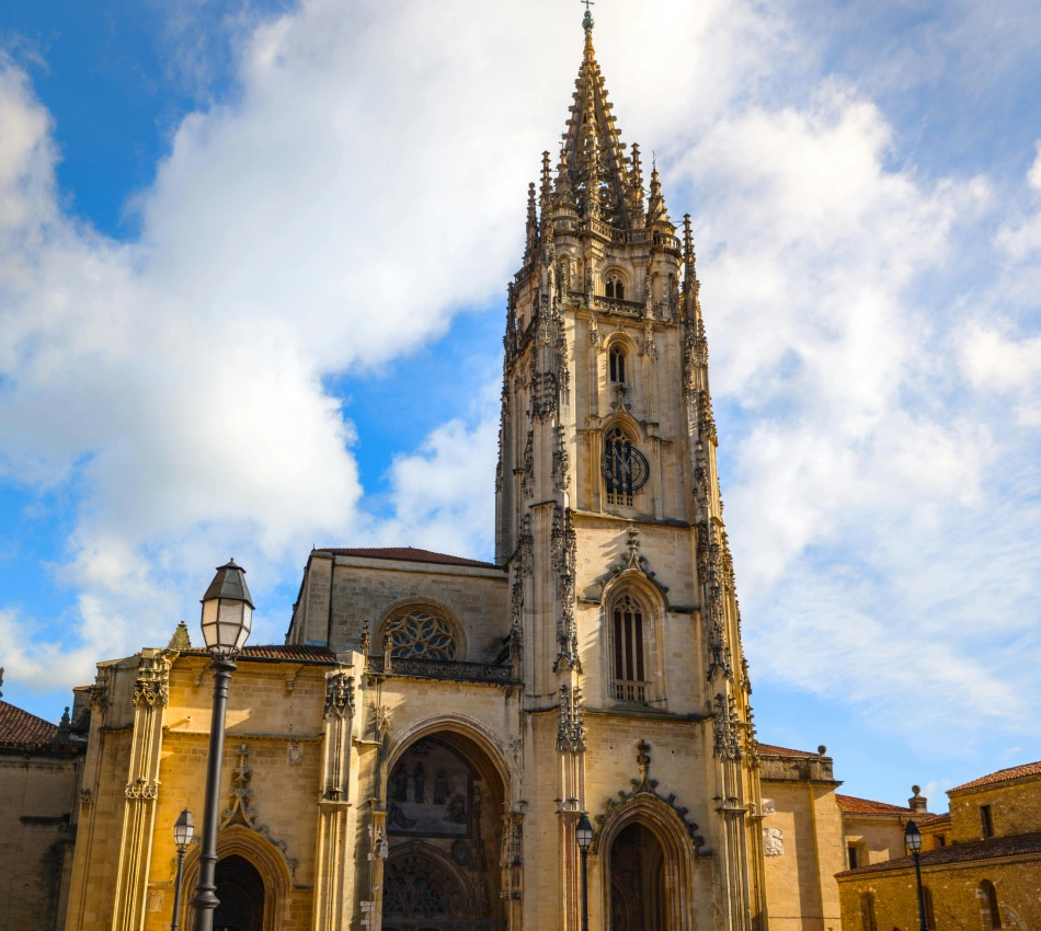 Torre de una iglesia g&oacute;tica con cielo azul y nubes, vista exterior.