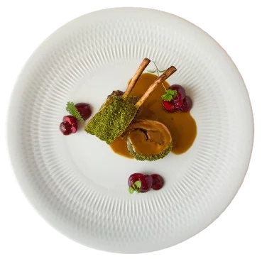 Plato gourmet con cordero, salsa y frambuesas, sobre plato blanco.