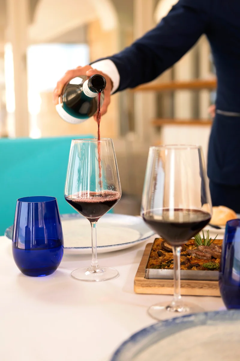 Sirviendo vino tinto desde una botella en una copa sobre una mesa.