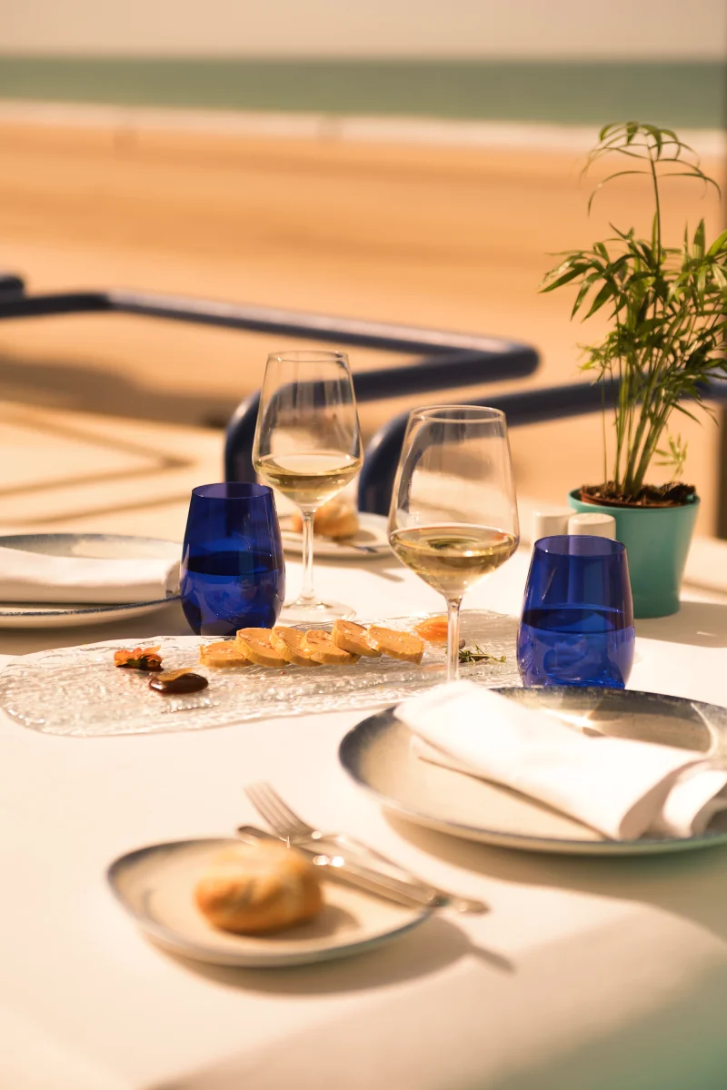Mesa con copas de vino y platos, luz cálida en terraza junto al mar