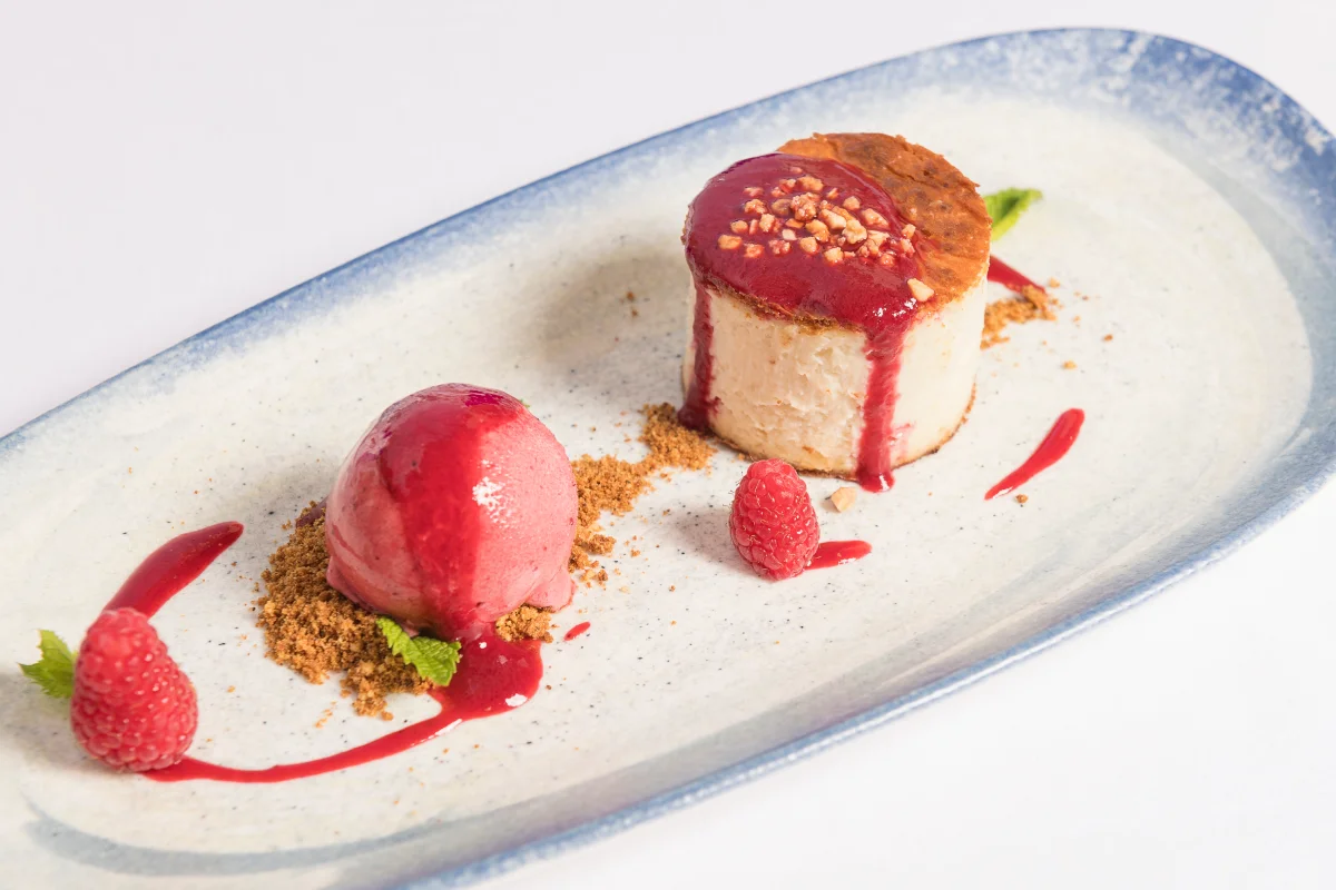 Postre de queso con gelatina roja, frambuesas y crumble en plato blanco