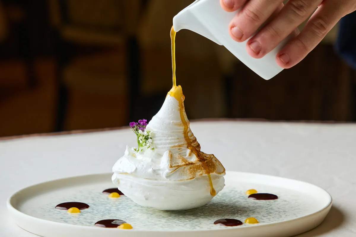 Mano vertiendo salsa amarilla sobre un postre blanco en plato blanco