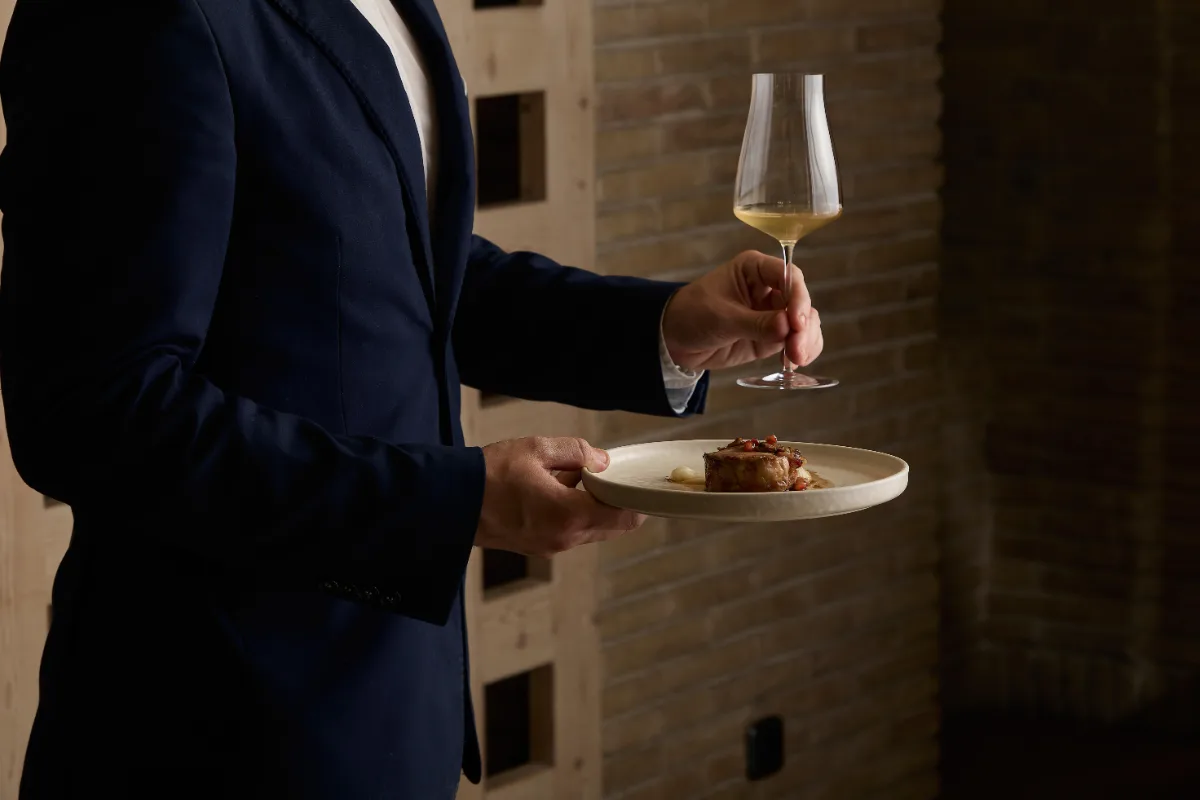 Camarero sirve vino y entrega un plato con comida en un restaurante.