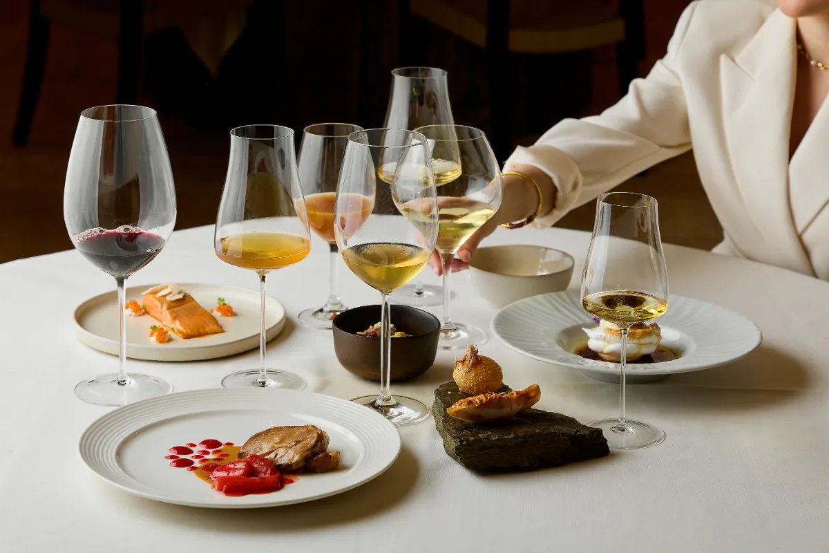 Mesa con platos y copas de vino; personas brindando en un restaurante.
