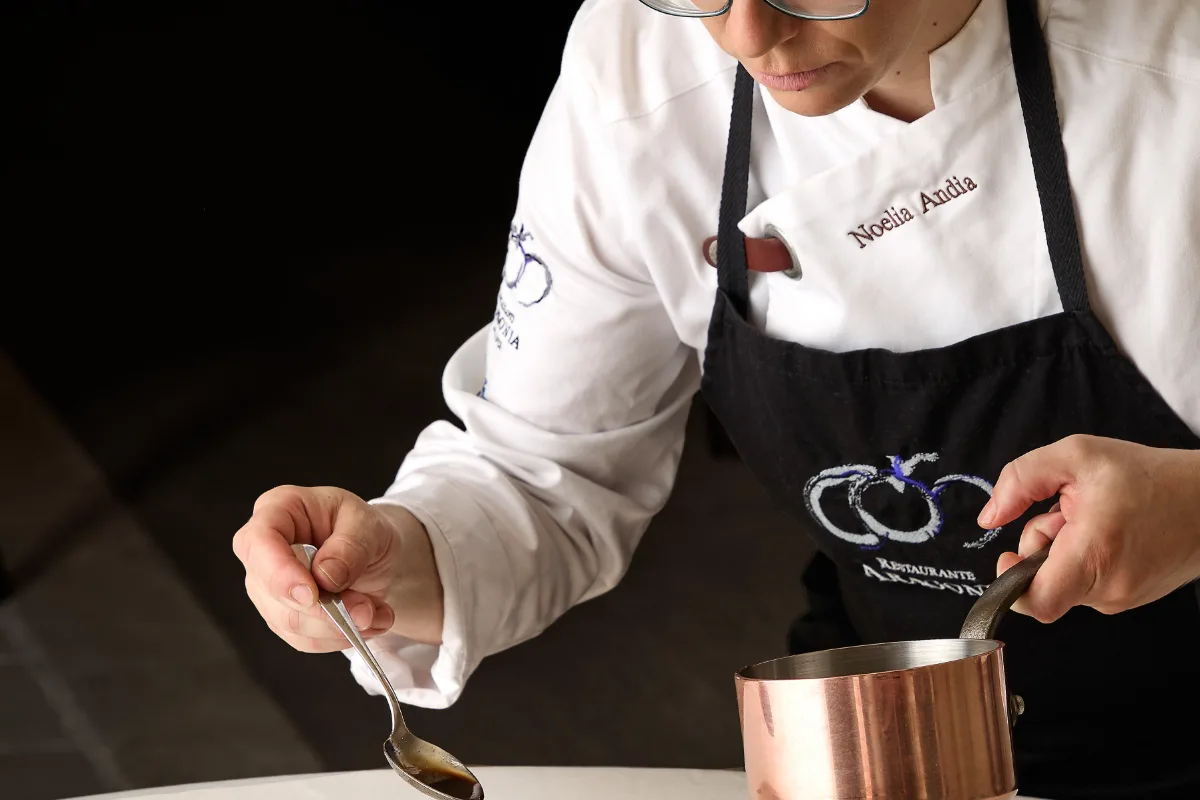 Chef con delantal negro preparando comida en una olla, en estudio.