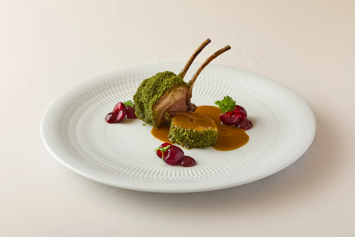 Plato gourmet con costilla de cordero, salsa y verduras verdes y rojas