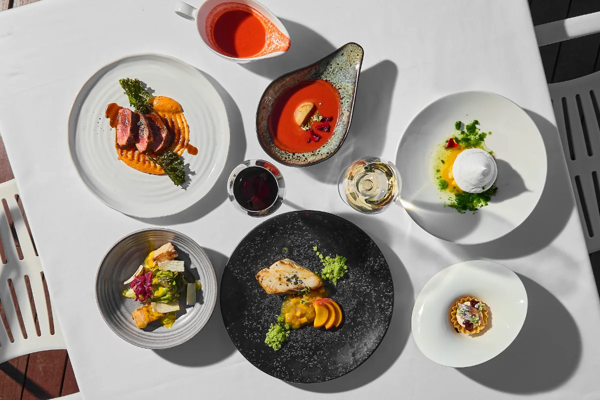 Mesa con platos gourmet: carnes, crema roja y guarniciones, vista cenital.
