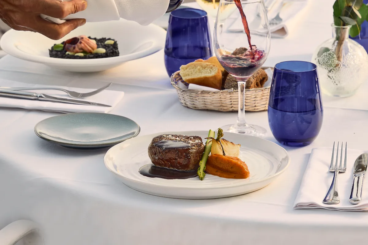Mesa con platos servidos, vino tinto y vajilla azul en una cena elegante