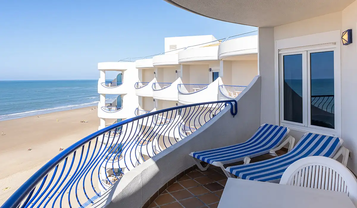 Balc&oacute;n con hamacas a rayas y vista al mar desde un hotel junto a playa