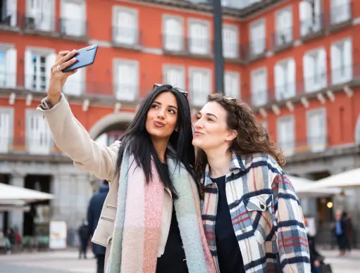Dos amigas se hacen selfie con el tel&eacute;fono en un patio de edificios rojos