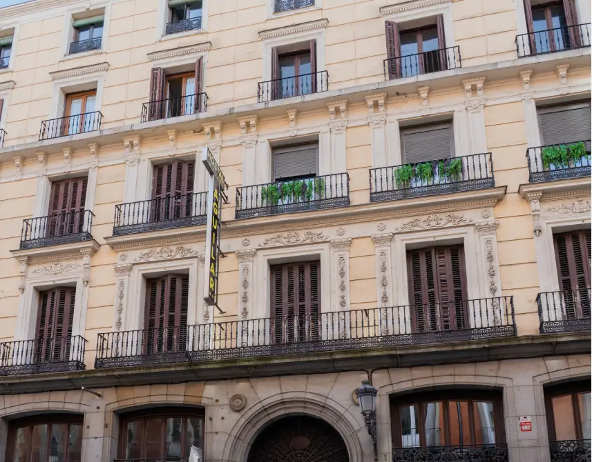 Fachada de edificio con balcones y persianas, fachada beige con ornamentos.