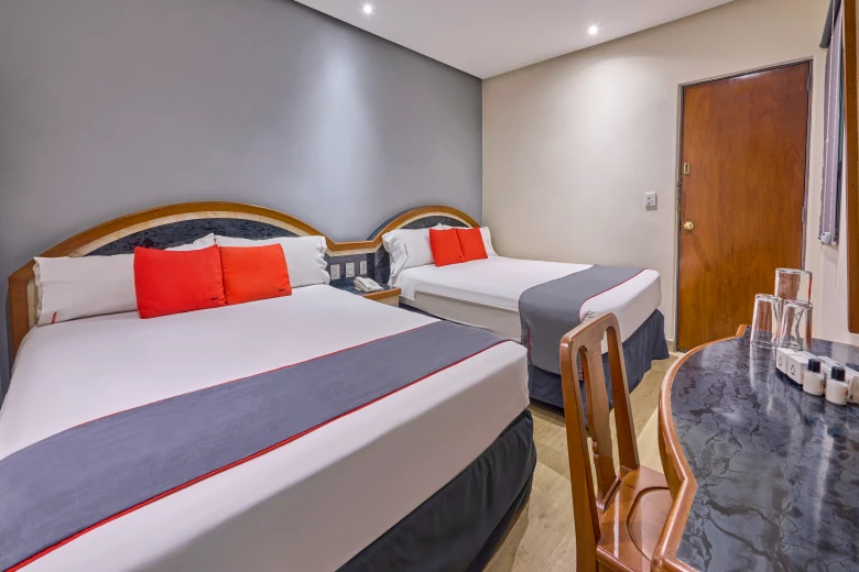 Habitaci&oacute;n con dos camas individuales, cojines rojos y mesa de noche.