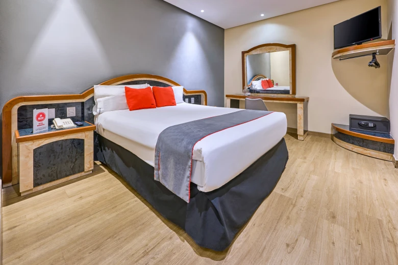 Dormitorio moderno con cama doble, cojines naranjas y TV en la pared