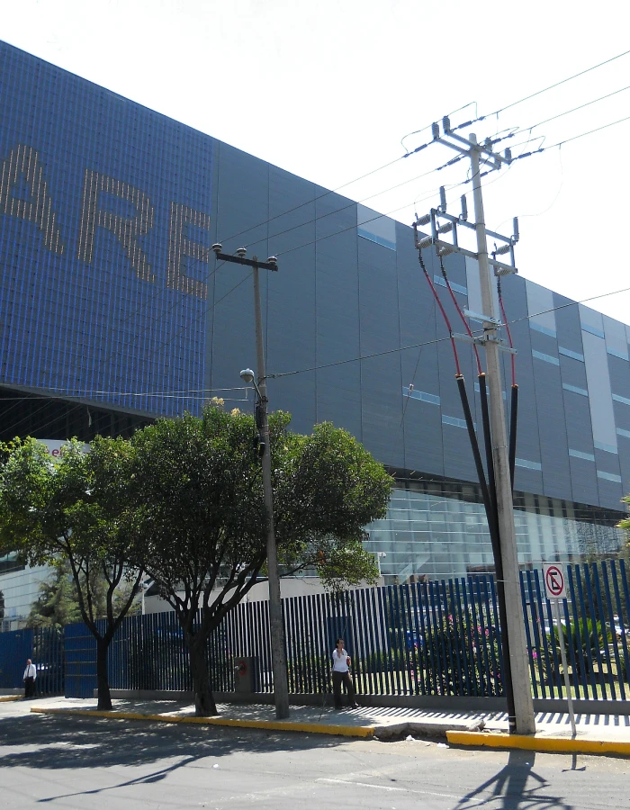 Edificio moderno con postes de energ&iacute;a y cables junto a un cerco met&aacute;lico