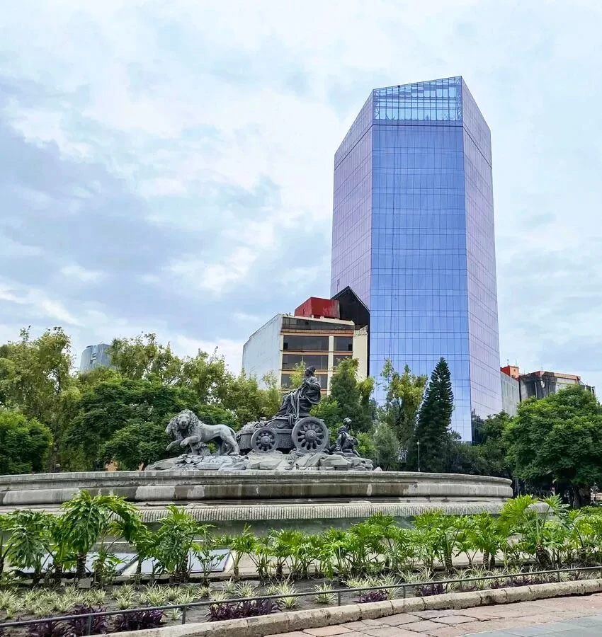 Monumento de bronce con estatuas y torre de cristal azul al fondo