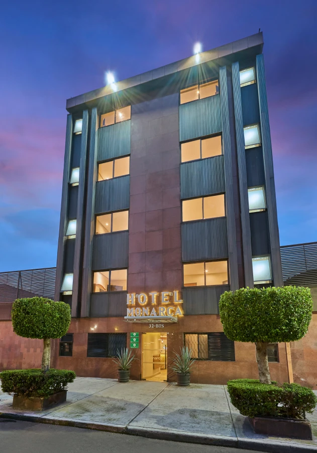 Fachada del Hotel Monarca al atardecer, con luces y plantas en la entrada