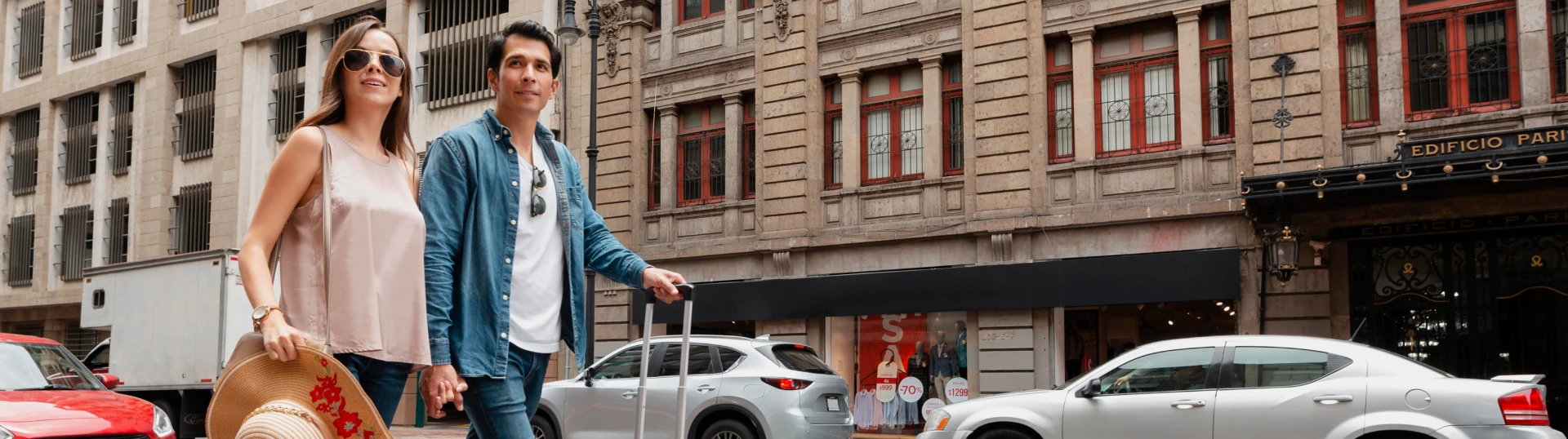Pareja pasea por la calle con edificios cl&aacute;sicos y coches estacionados, en verano.