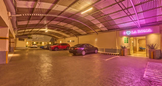 Aparcamiento con coches bajo techo y letrero luminoso &ldquo;LA ROMA&rdquo;.