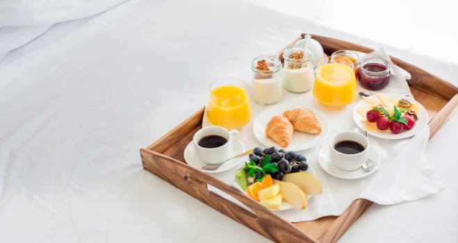 Bandeja con desayuno: croissant, frutas, yogur y jugos en vasos y cuencos.