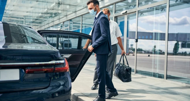 Hombre con mascarilla camina en el aeropuerto junto a un coche negro