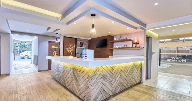 Recepci&oacute;n moderna con mostrador de madera en &aacute;ngulo, luces y TV.