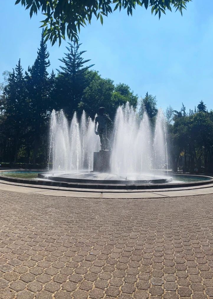 Fuente con chorros de agua en un parque con &aacute;rboles y cielo azul