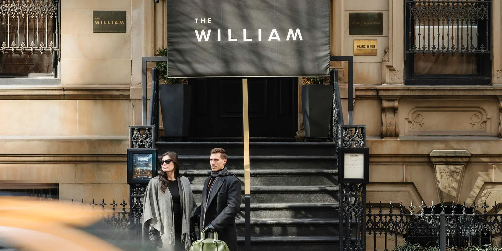 Two people stand outside “The William” theater entrance with a large banner