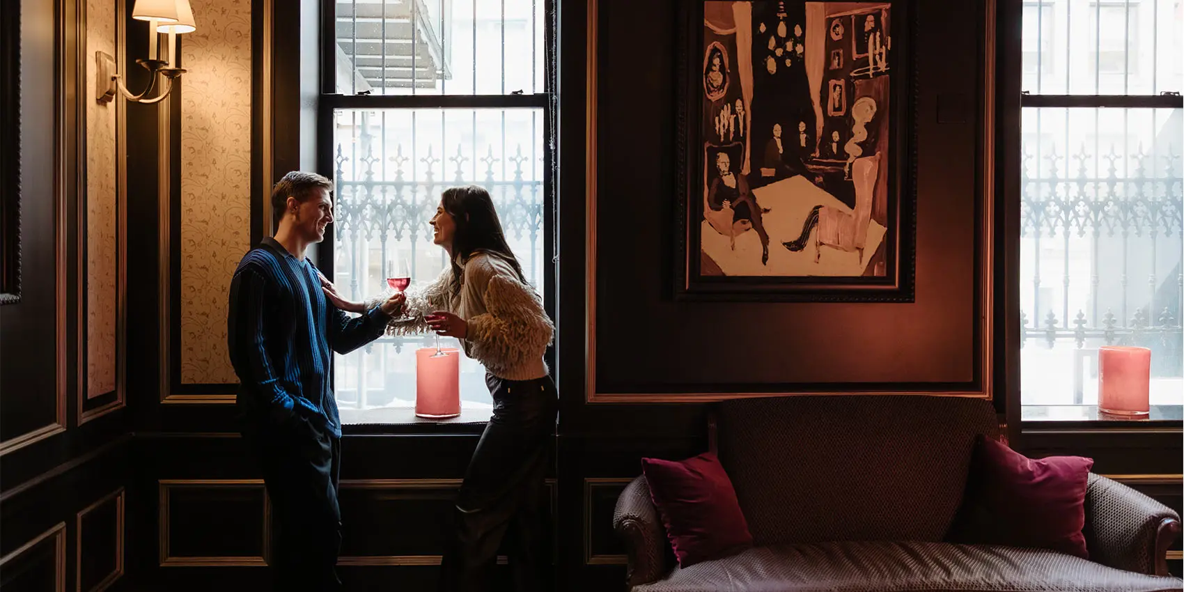 Couple toasting wine in a cozy lounge by large windows and artwork