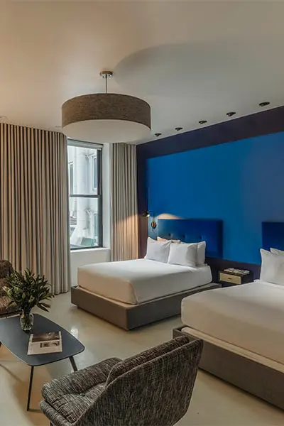 Modern hotel room with blue accent wall, beds, and lounge seating by window