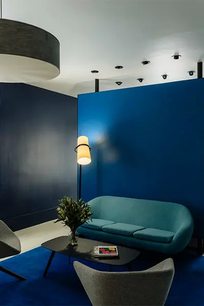 Modern room with blue walls, curved teal sofa, tables, and ceiling lights