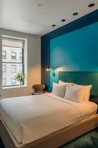 Modern bedroom with blue accent wall, large window, and neatly made bed