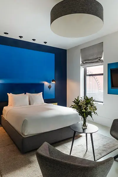 Modern hotel room with blue accent wall, bed, and ceiling light fixtures
