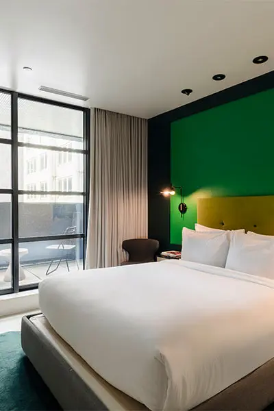 Modern hotel room with large bed, colorful accent wall, and balcony view