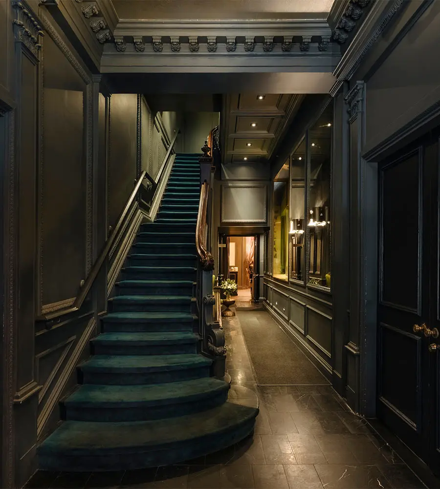 Elegant hallway with dark walls, ornate molding, and green-carpeted staircase
