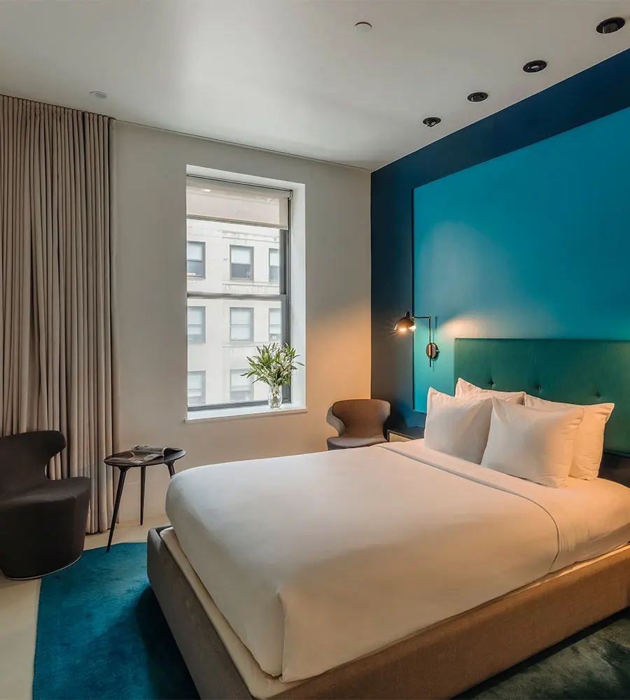 Modern hotel room with a large bed, blue accent wall, and window view