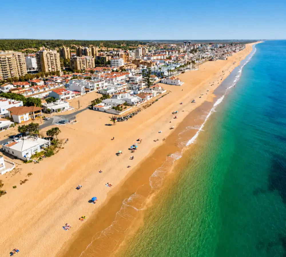 Vista a&eacute;rea de una playa con casas y ba&ntilde;istas junto al mar.