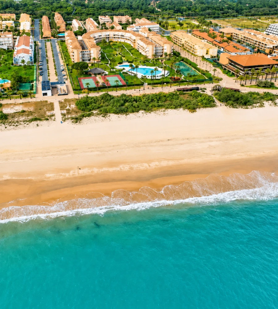 Vista a&eacute;rea de una playa tropical con olas y complejo hotelero entre jardines