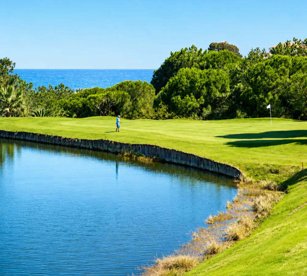 Campo de golf junto a un estanque, con &aacute;rboles y el mar al fondo