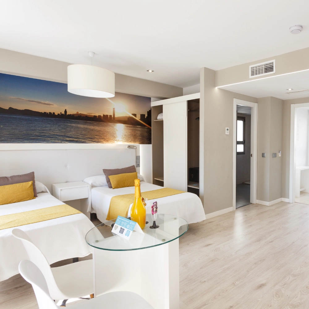 Sala de hotel moderna con camas, mesa de cristal y l&aacute;mpara de techo
