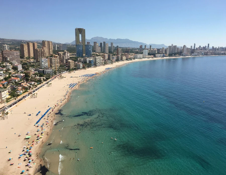 Vista a&eacute;rea de una playa urbana con edificios y mar turquesa al atardecer