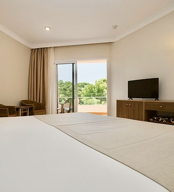 Habitaci&oacute;n con cama, TV y salida a balc&oacute;n con vista al jard&iacute;n