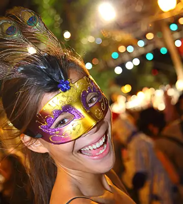 Mujer sonriente con antifaz de carnaval p&uacute;rpura y dorado en la calle.