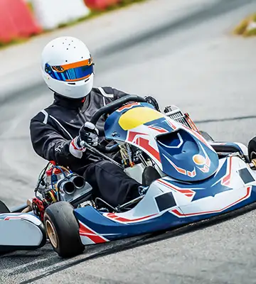 Piloto de kart con casco blanco y auto azul, rojo y blanco en pista